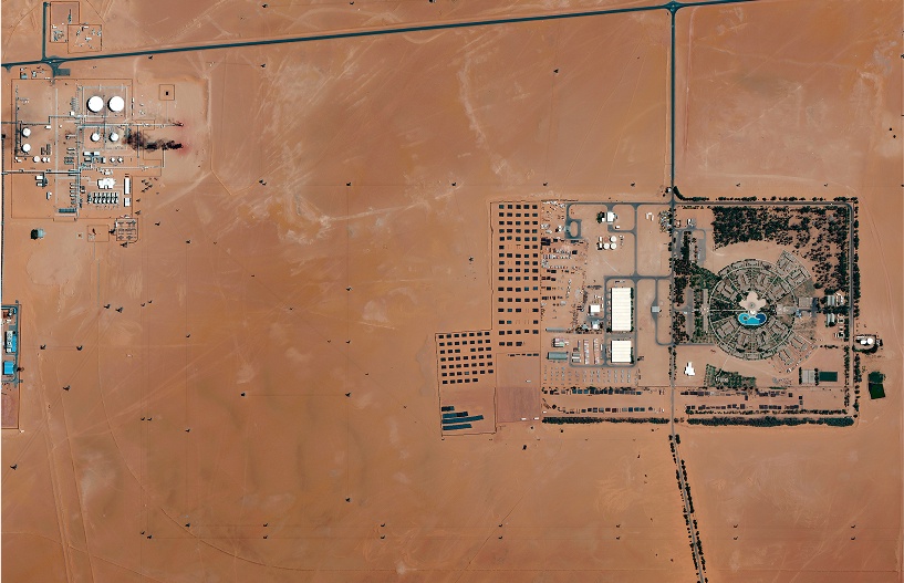 Satellite image of a large-scale oil and gas field with multiple well pads, processing facilities, and storage tanks in a desert region, highlighting remote monitoring capabilities.